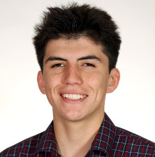 A young man wearing a plaid shirt smiles brightly at the camera, exuding a cheerful and friendly demeanor.